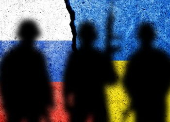 Shadows of soldiers against flags of Russia and Ukraine painted on a concrete wall.