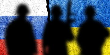Shadows of soldiers against flags of Russia and Ukraine painted on a concrete wall.